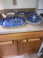 Full view of all items on countertop showing five dinner plates stacked, large and small platters, bowls, and tea cup with saucer.