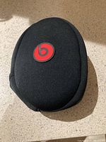 Black semi-hard shell carrying case with red Beats logo on top, placed on a beige surface.