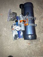 Blue Celestron telescope optical tube with attached focuser and small parts in plastic bags placed beside it on the floor.