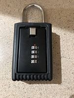 Front view of black combination padlock with visible four numeric dials and metal shackle.