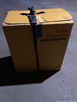 Yellow Kodak Ektagraphic slide projector box closed, strapped with blue buckle strap
