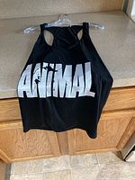 Black sleeveless tank top with large white ANIMAL text on front, hung on a hanger.