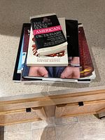 Stack of four old books on a countertop, top book is 'The Random House American Dictionary' with a black, white, and red cover and text indicating a comprehensive dictionary annotated by Burton Raffel.
