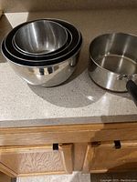 Four nested stainless steel mixing bowls and one stainless steel saucepan on countertop.