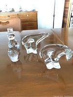 Photo showing three clear blown glass figures on a wooden table: a snowman and two polar bears.