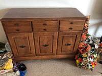Full front view of wooden buffet with three drawers above and three cabinet doors below, showing minor wear, medium brown finish, and metal handles.