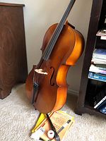 Cello standing upright with bow, recorder and sheet music on floor