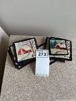 Stack of nine handcrafted hooked mat coasters with winter-themed designs including snow-covered houses and trees, shown with MaxSold tag for lot identification.