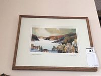 Framed watercolour painting titled "Frozen Lake" showing the full frame and mat with signatures visible below painting.