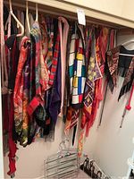 Wide view of scarves hung on hangers showing various colors, patterns, including plaid wool, silk scarfs with geometric and abstract prints