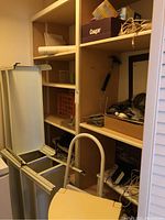 Wide shot of shelving units filled with miscellaneous items including a hammer, picture frame, cords, and boxes. Visible step stool in foreground.