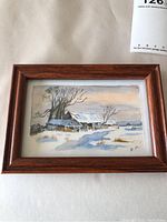 Framed watercolor painting showing a snow-covered farm landscape with barns and trees, sign R.M. visible.