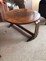 Side view of the round walnut veneer side table showing the curved legs and stretcher support.