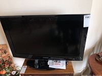 Full view of Samsung 32 inch flat screen TV on wooden surface with remote and base stand in front.