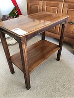 Rectangular wooden table with open lower shelf and warm brown finish, minor surface wear visible.