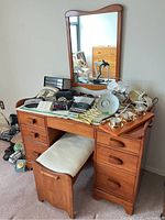 Full view of solid wood vanity with various items on top, showing mirror, drawers, and stool underneath