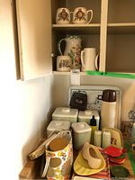 Full view of vintage kitchen items in cabinet including canisters, thermos, trays, mugs, and jugs.