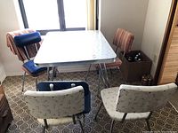 Vintage rectangular table with white patterned laminate top and chrome legs surrounded by four chairs of various upholstery styles.
