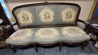 Front view of antique French Victorian settee showing detailed upholstery with pastoral scenes and floral designs on seat and backrest.