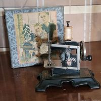 Miniature antique sewing machine and original decorated box with illustration in background.