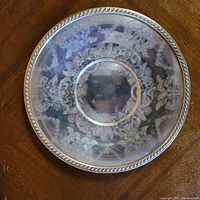 Top down photo showing full face of round Victorian silver plated plate with detailed floral and scroll engraved patterns and rope border.