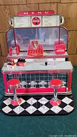 Front view of Coca-Cola fountain miniature with counter, two stools, and soda crates