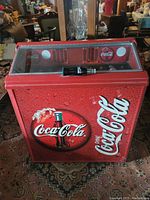 Front view of the Coca-Cola stacker refrigerator featuring the red Coca-Cola branding with water droplet design and a classic glass Coke bottle illustration.