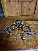 Photo showing several bracelets and two necklaces with different metallic finishes and rhinestones arranged on a wooden surface.