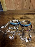 Photo shows multiple pieces of costume jewelry including bracelets and necklaces laid out on wooden surface.