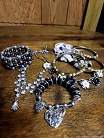 Photo showing six pieces of assorted costume jewelry including a multi-strand beaded bracelet, rhinestone necklace, and several bangles with pearl and floral motifs in black, white, and silver tones.