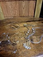 Image showing five assorted chain necklaces arranged on a wooden surface, including gold and silver tones with some featuring faux pearl bead decorations.