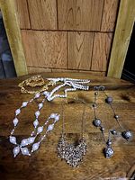 Image of five different costume necklaces displayed on a wooden surface with a wooden background, showcasing different bead styles and metal finishes.