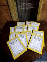 Image shows 13 vintage National Geographic magazines arranged on a wooden table. Each magazine features the distinctive yellow frame and black text listing contents on the cover.