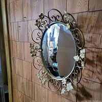 Oval decorative mirror with ornate metal frame featuring floral and leaf accents.