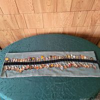 Full view of entire collection of roughly 40 souvenir spoons laid out on a green textured tablecloth and displayed on a fabric holder.