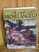 Photograph of the front cover of the book showing the title 'The Complete Work of Michelangelo' with artwork depicting a figure in purple hues.