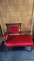 Front view of Victorian Eastlake settee showing carved wooden frame and red upholstered seat and backrest with tufted buttons.