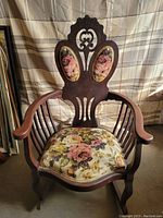 Front view of Victorian high back rocking chair showing carved wooden frame and floral seat and back upholstery.
