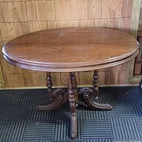 Oval Victorian wooden table with ornate pedestal base and four curved legs, photographed from above at an angle.