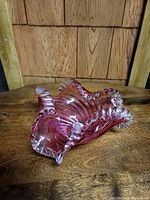 Photo showing the vintage cranberry glass candy dish with ruffled edges on a wooden surface.