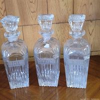 Photo showing three crystal decanters with decorative cut facets and stoppers.