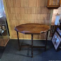 Full view of vintage wooden side table with octagonal scalloped top and turned legs against wood wall background.