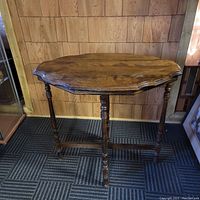 Full view of vintage wooden side table against wood-paneled wall on patterned carpet