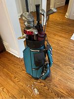 Full set of golf clubs including putters and other clubs in blue golf bag on wooden floor with tees and balls in front
