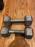 Pair of gray metal 8 pound dumbbells with hexagonal ends shown resting on a wood floor. Some rust spots are visible on surfaces.