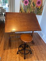 Front view of adjustable drafting table with stool (stool not included) showing tilt surface