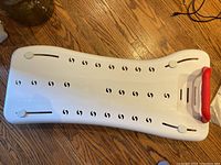 Top view of the white adjustable bathtub safety shelf showing rows of ventilation holes and red safety handle at one end.