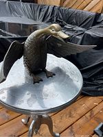Bronze duck sculpture viewed from front showing extended wings, webbed feet, and detailed feathers on a metal stand.