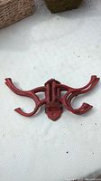 Red cast iron coat rack with five arms pivoted outward, placed on a white textured surface.