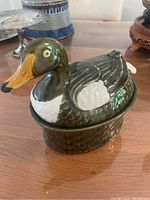 Front and side view of the green glazed ceramic duck-shaped dish with detailed feathers, white patches on wings, and yellow beak.